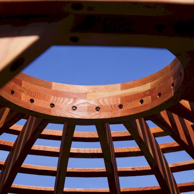 Wooden Dome Pergola (Options: 16' Diameter, with Deck in Coffee Stain, Douglas-fir, Open Roof with Slats at 6", 9' Posts, No Electrical Wiring Trim, 6-Post Anchor Kit for Concrete, Transparent Premium Sealant). Photo Also shows a Round Picnic Table and a Rory's Swing Set in Background.
