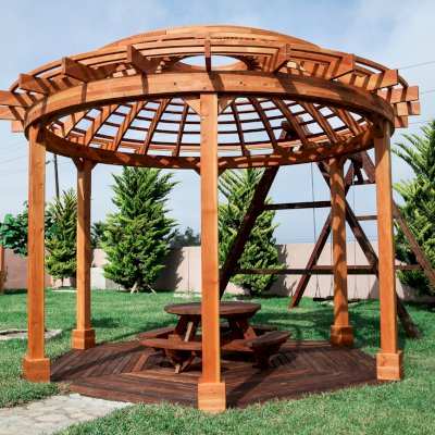 Wooden Dome Pergola (Options: 16' Diameter, with Deck in Coffee Stain, Douglas-fir, Open Roof with Slats at 6", 9' Posts, No Electrical Wiring Trim, 6-Post Anchor Kit for Concrete, Transparent Premium Sealant). Photo Also shows a Round Picnic Table and a Rory's Swing Set in Background.