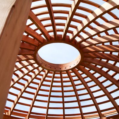 Wooden Dome Pergola (Options: 16' Diameter, with Deck in Coffee Stain, Douglas-fir, Open Roof with Slats at 6", 9' Posts, No Electrical Wiring Trim, 6-Post Anchor Kit for Concrete, Transparent Premium Sealant). Photo Also shows a Round Picnic Table and a Rory's Swing Set in Background.