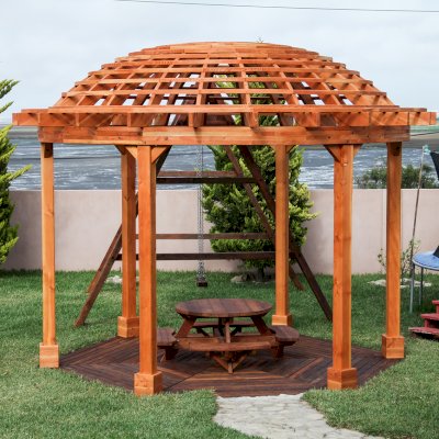 Wooden Dome Pergola (Options: 16' Diameter, with Deck in Coffee Stain, Douglas-fir, Open Roof with Slats at 6", 9' Posts, No Electrical Wiring Trim, 6-Post Anchor Kit for Concrete, Transparent Premium Sealant). Photo Also shows a Round Picnic Table and a Rory's Swing Set in Background.