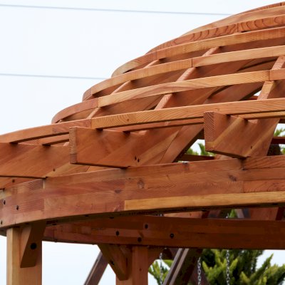 Wooden Dome Pergola (Options: 16' Diameter, with Deck in Coffee Stain, Douglas-fir, Open Roof with Slats at 6", 9' Posts, No Electrical Wiring Trim, 6-Post Anchor Kit for Concrete, Transparent Premium Sealant). Photo Also shows a Round Picnic Table and a Rory's Swing Set in Background.