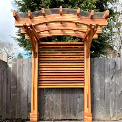Two-Post Arched Wood Arbor (Options: 6' x 3', Mosaic Redwood, 7' Posts Height, 2-Post anchor Kit for High-Wind, Custom Louvered Half Height Privacy Wall Added by Customer Request, Vertical Post Decorative Trims, with Rain Guard, Transparent Premium Sealant). Photo Courtesy of E. Baechler of Portland, Oregon.